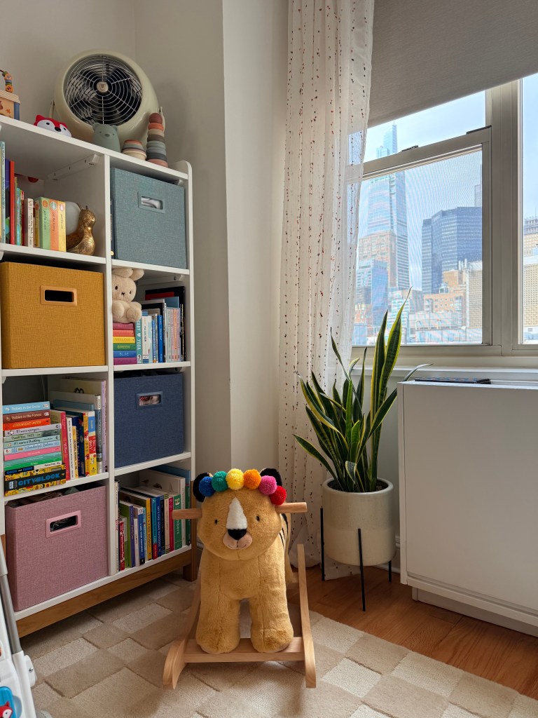 image of a nursery corner with black out shades rolled slightly down and sheer curtains on the sides